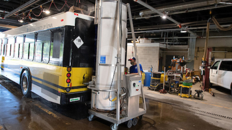 transit bus in black and gold color scheme being cleaned by machine and employee