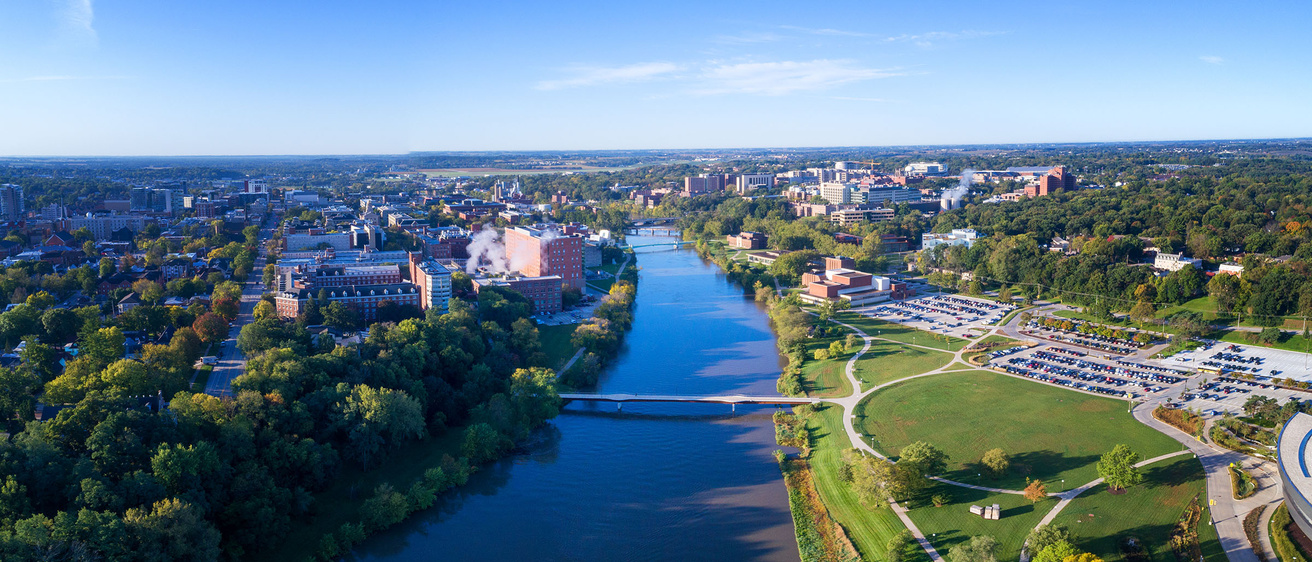 Iowa River shown center with clear blue sky and green grass along river with main campus east shown left and medical/arts campus west shown right