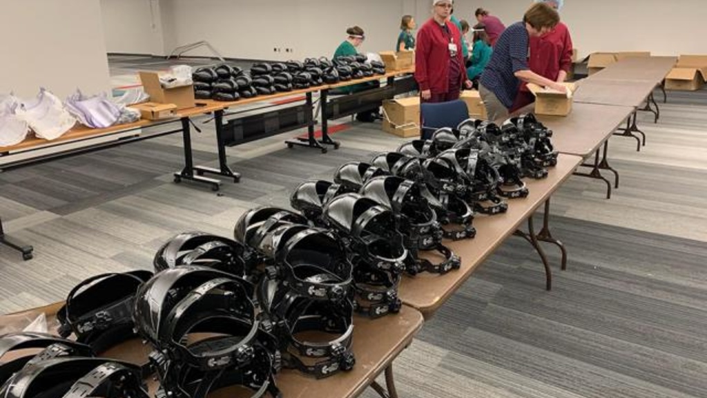 Rows of protective face shields on tables with employees unboxing in the background