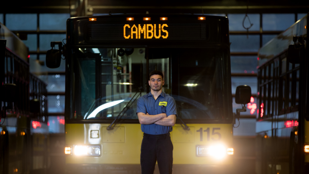 person wearing blue uniform shirt standing in front of bus with headlights on