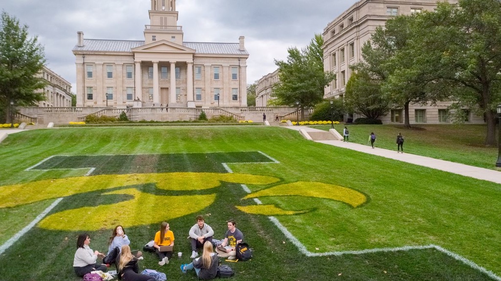 students sitting on central campus lawn with Old Capitol in the background and tiger hawk painted on grass