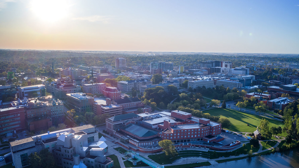 image of campus from drone with river and pedestrian bridge in center during sunrise